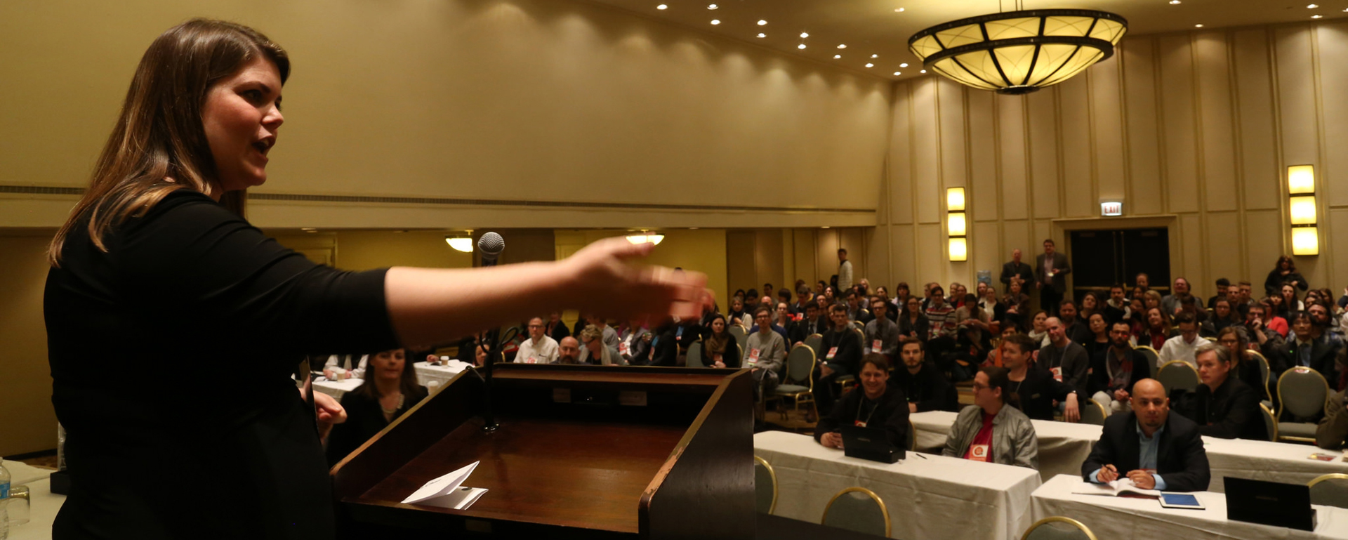A woman with brown hair lectures to an audience at the MWXX conference.
