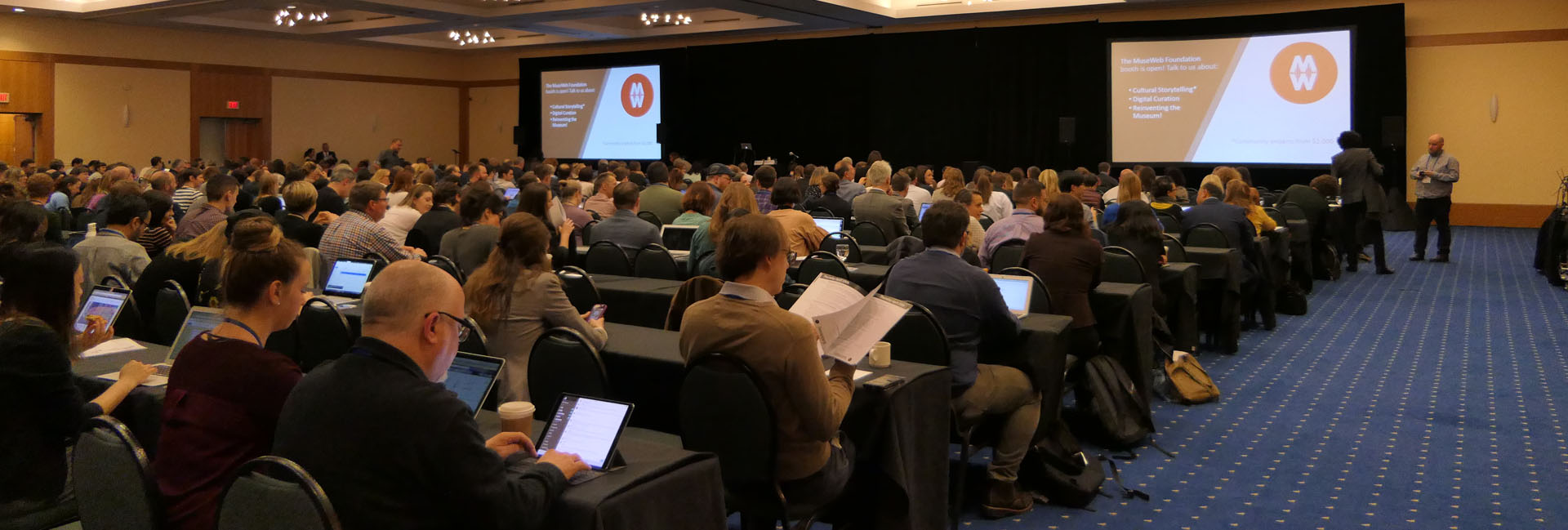 A crowded room full of conference participants, waiting for a session to begin.