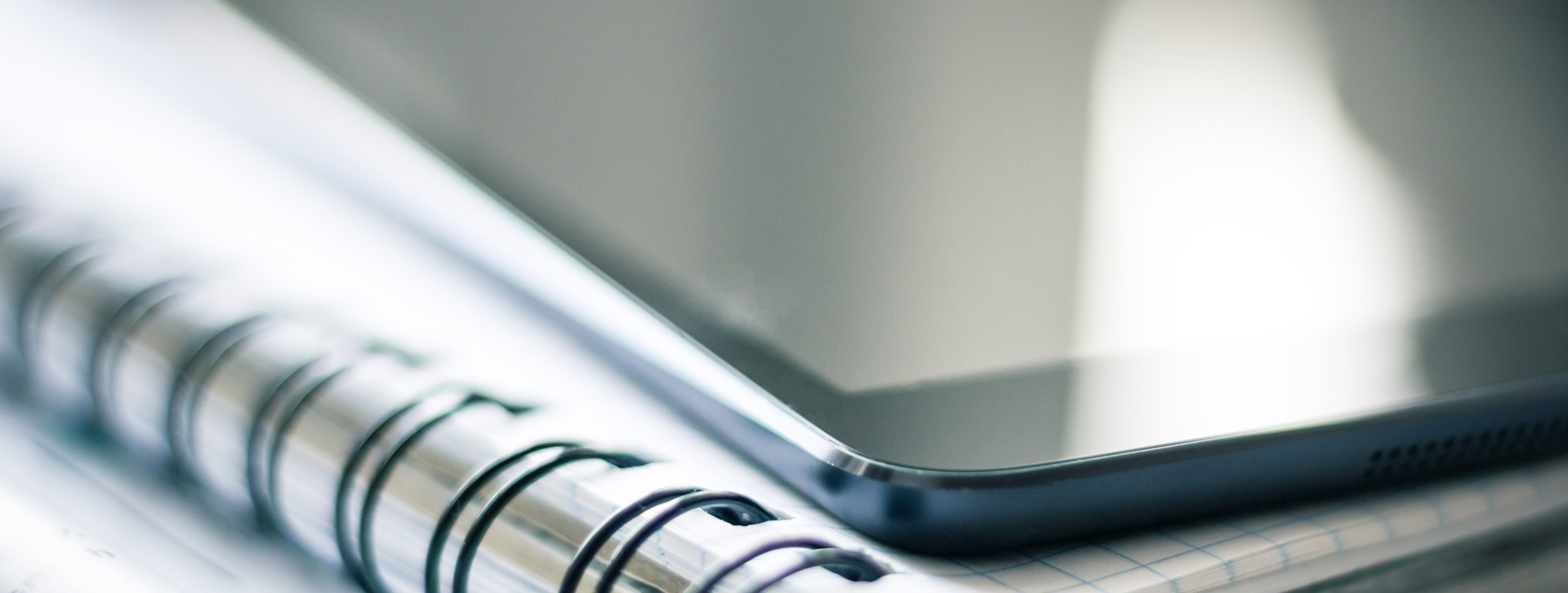 The front of an iPad or tablet on top of a number of spiral notebooks. 