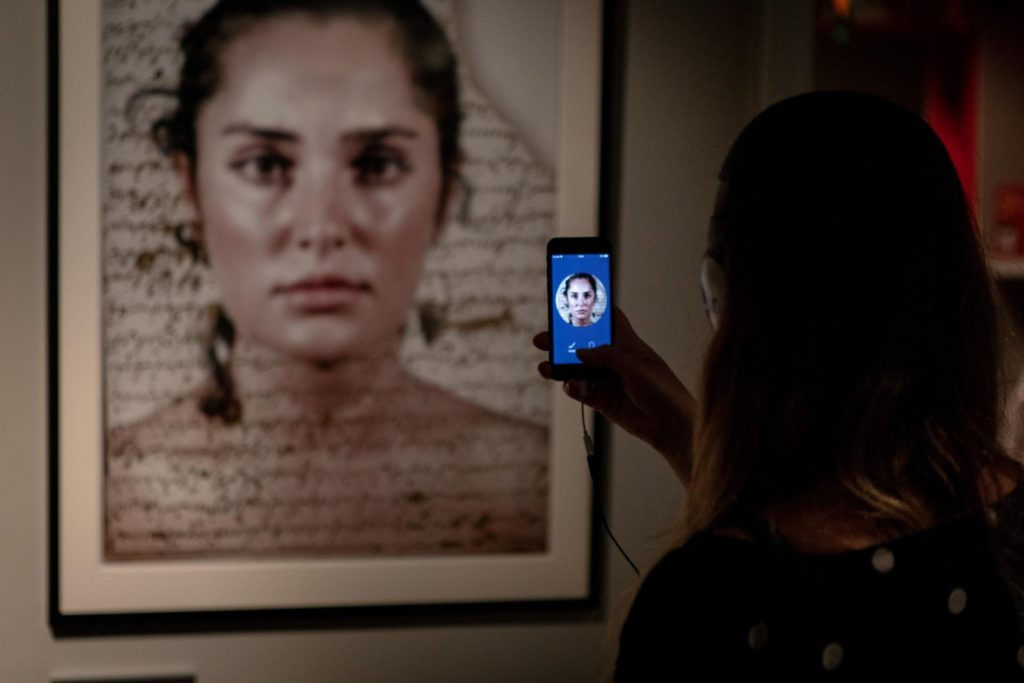 A woman holds a phone up to a photographs and takes a picture. 