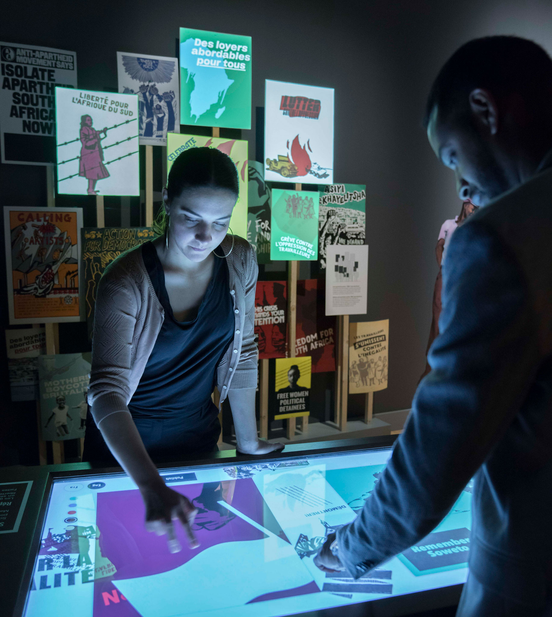 A woman leans over a computer touchscreen in the background, while a male stands in the foreground.