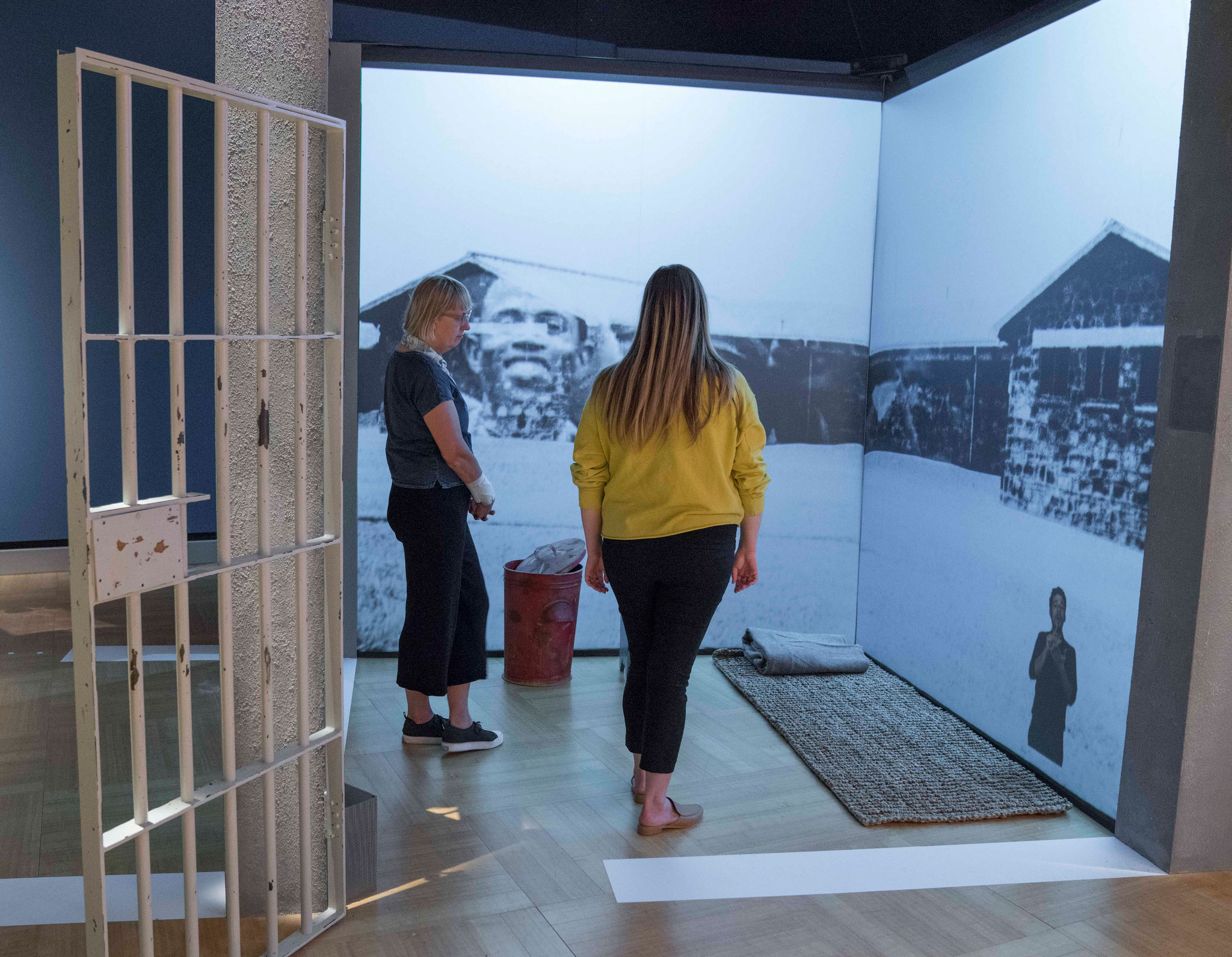 Two women stand inside a recreation of a jail cell.