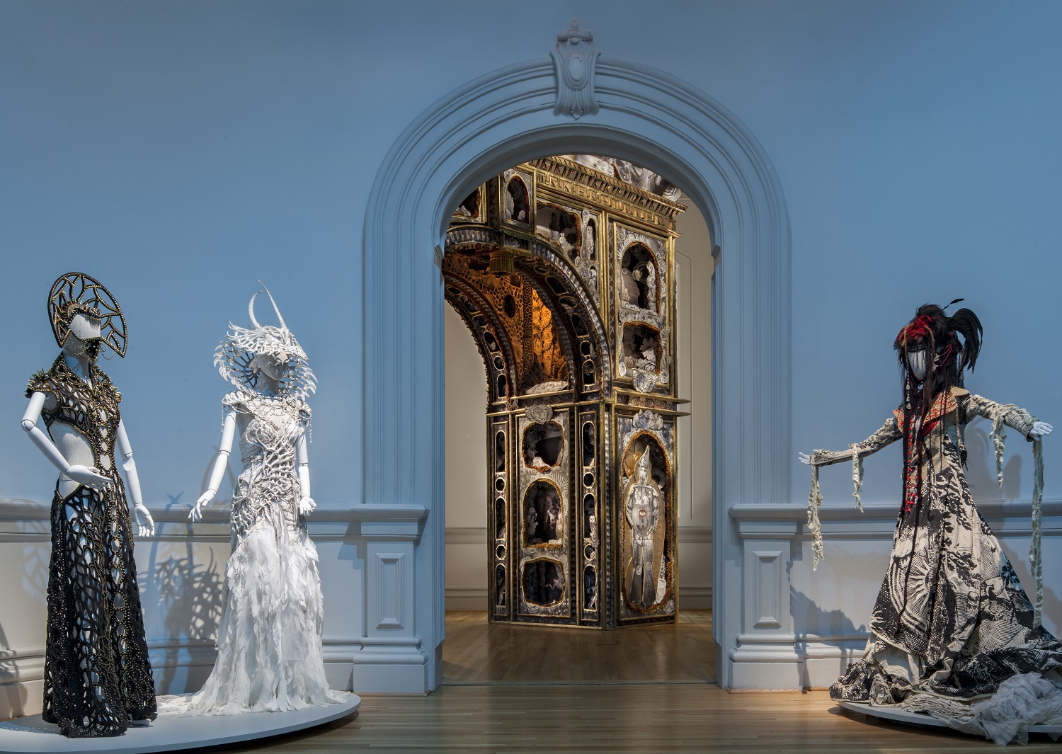 Three long dress costumes on mannequins flank an arched doorway